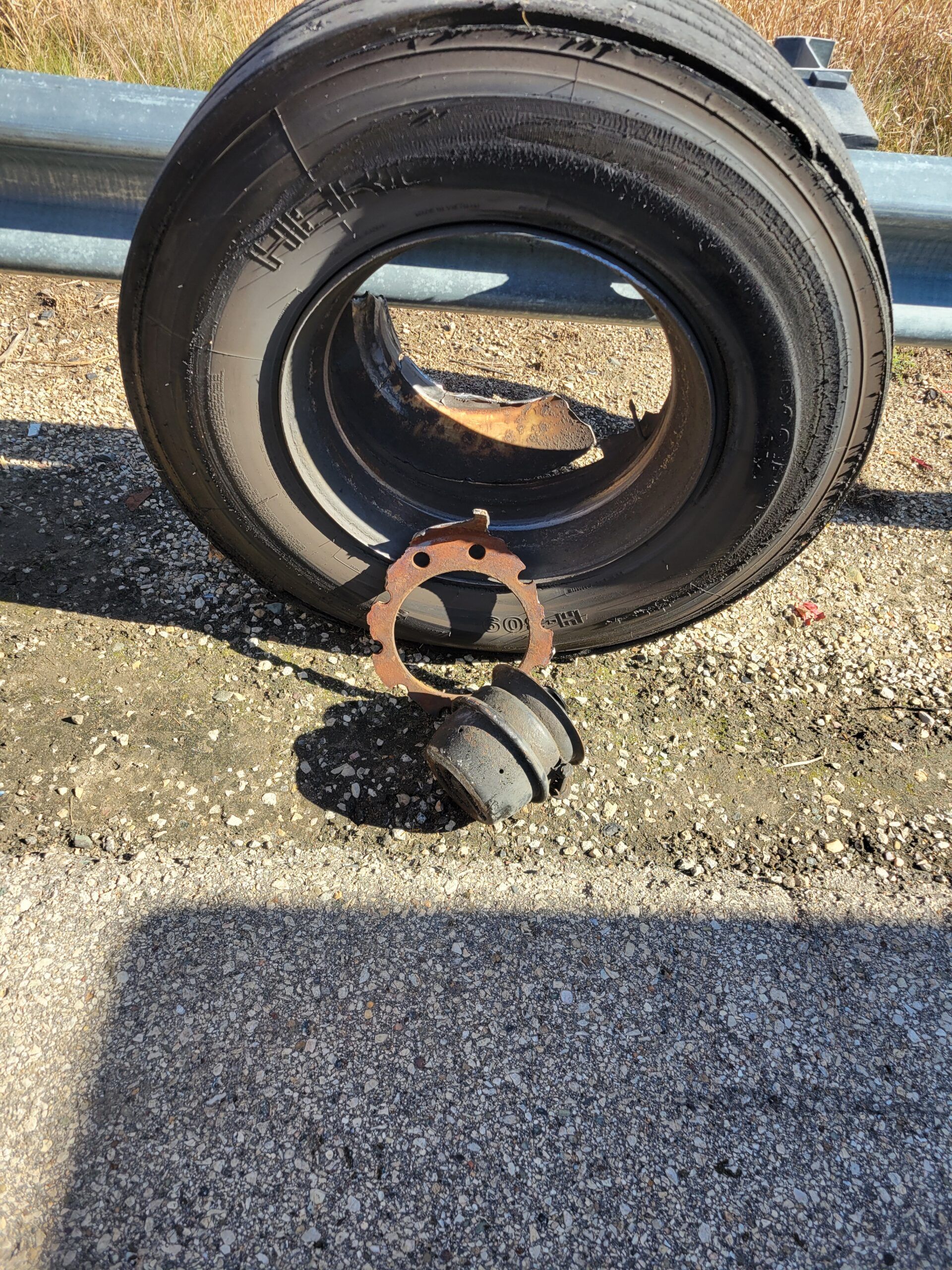 Black tire on pavement with a rusted brake drum and loose parts in front of it