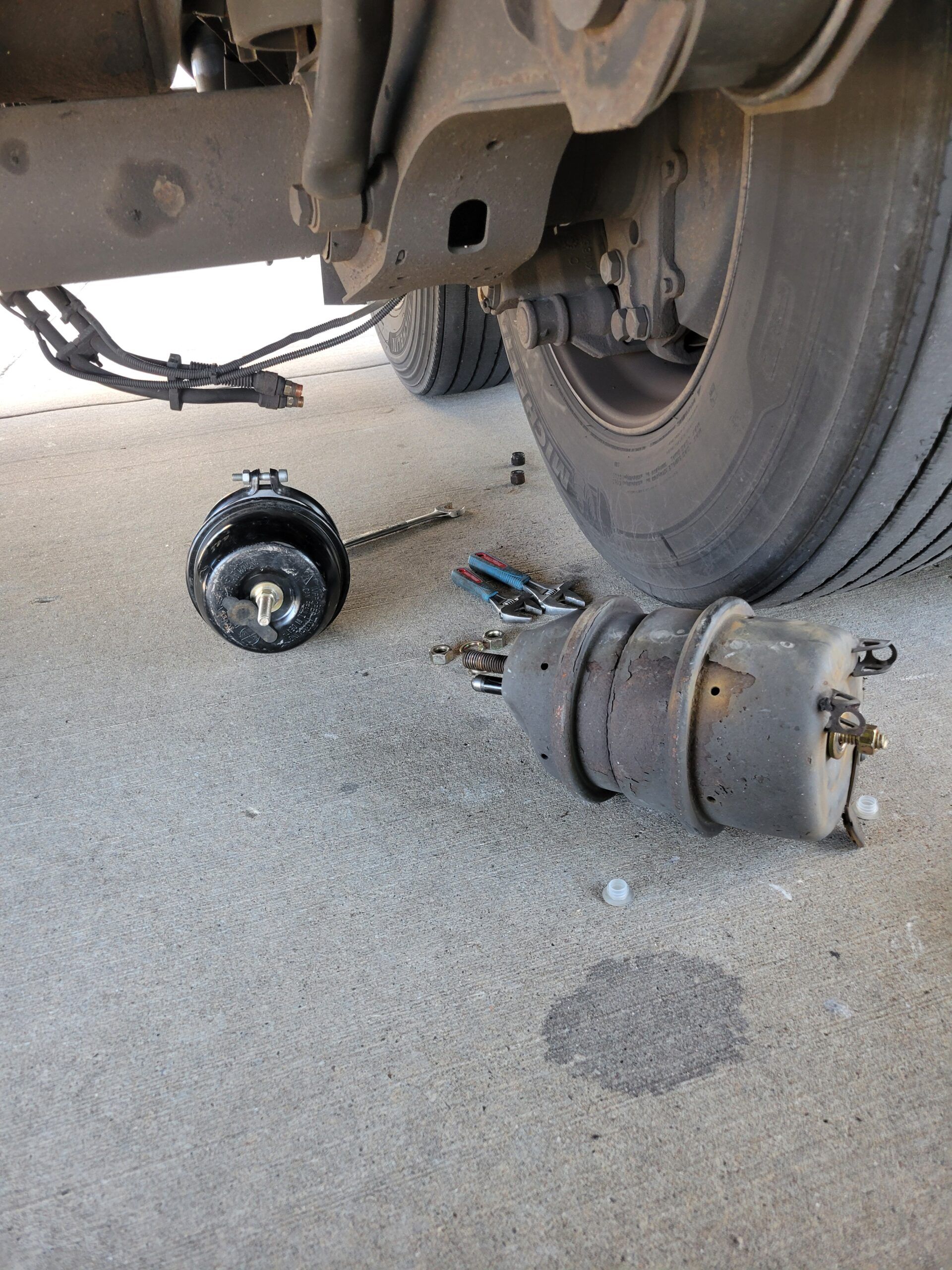 Underneath a truck, a damaged axle and wheel assembly lie broken on the pavement.