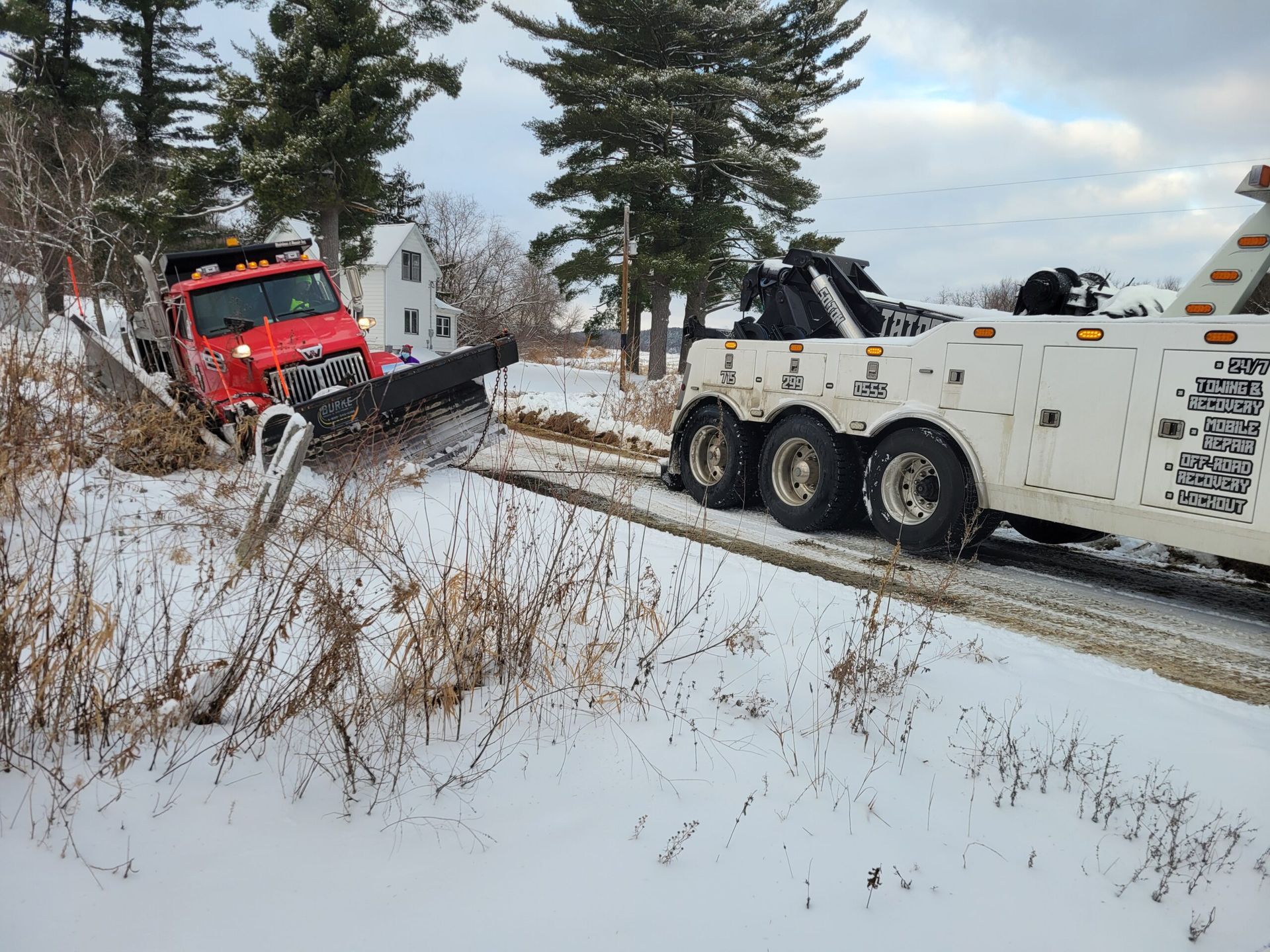 Red tow truck pulled into snowy ditch beside white tow truck on a winter road
