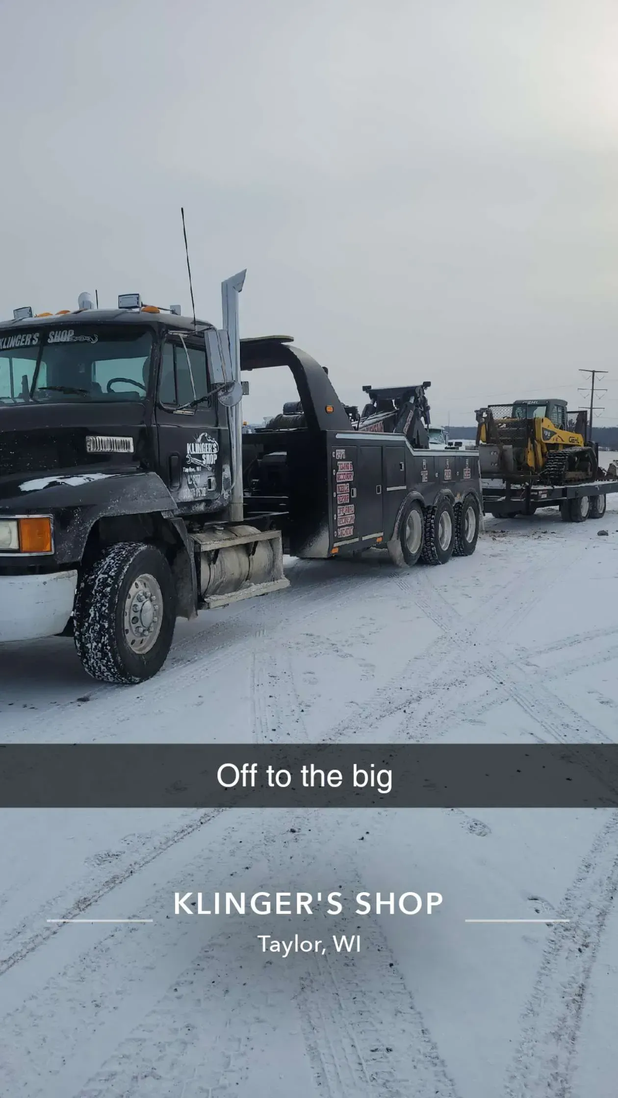 Tow truck hauling a car on a snowy road, with other vehicles lined up behind it.