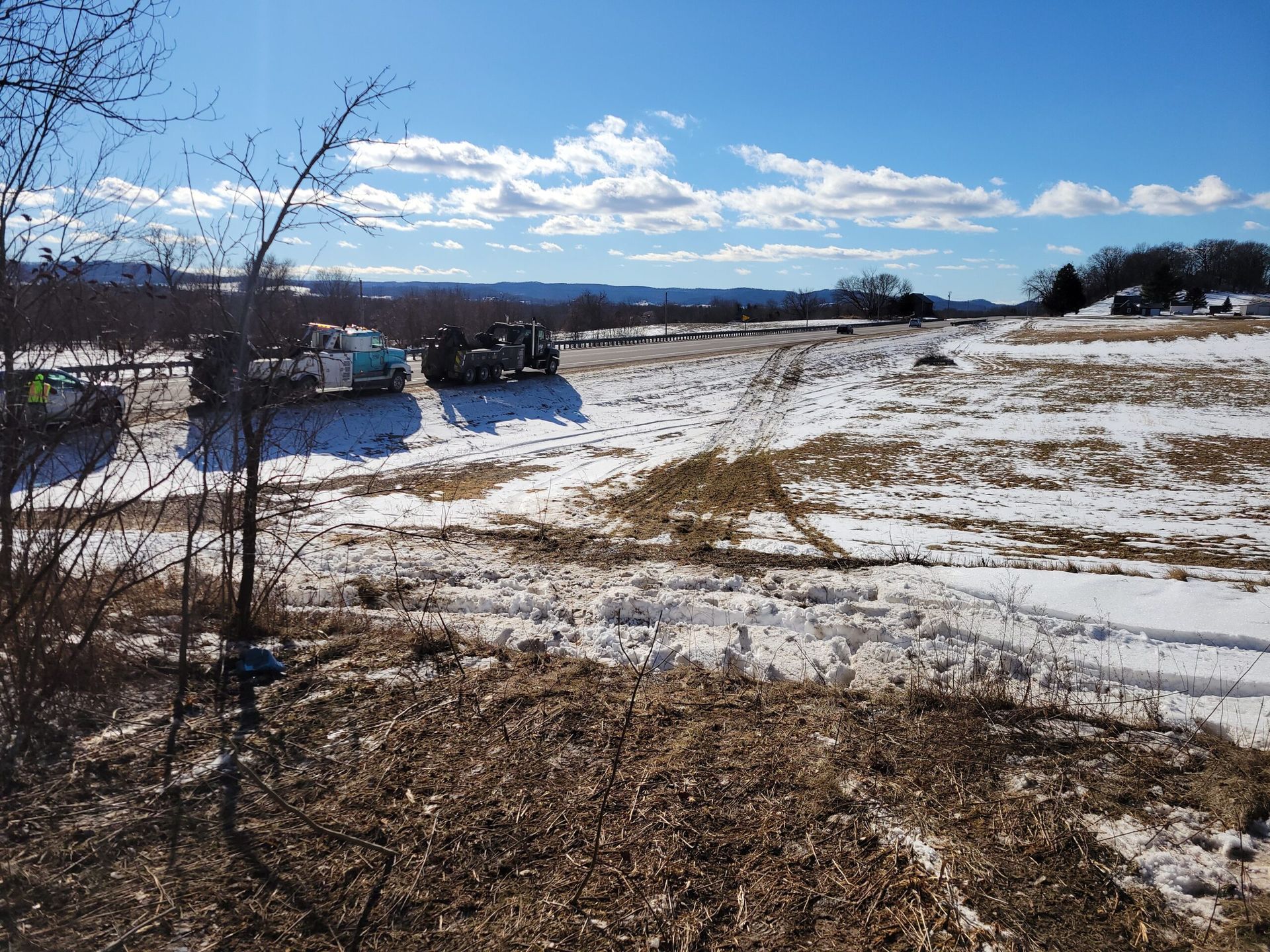 Snow-covered field under a bright blue sky, with bare trees and a road on the left.