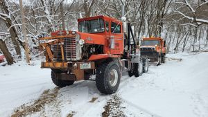 Orange snowplow trucks clearing a snowy road in a wooded area