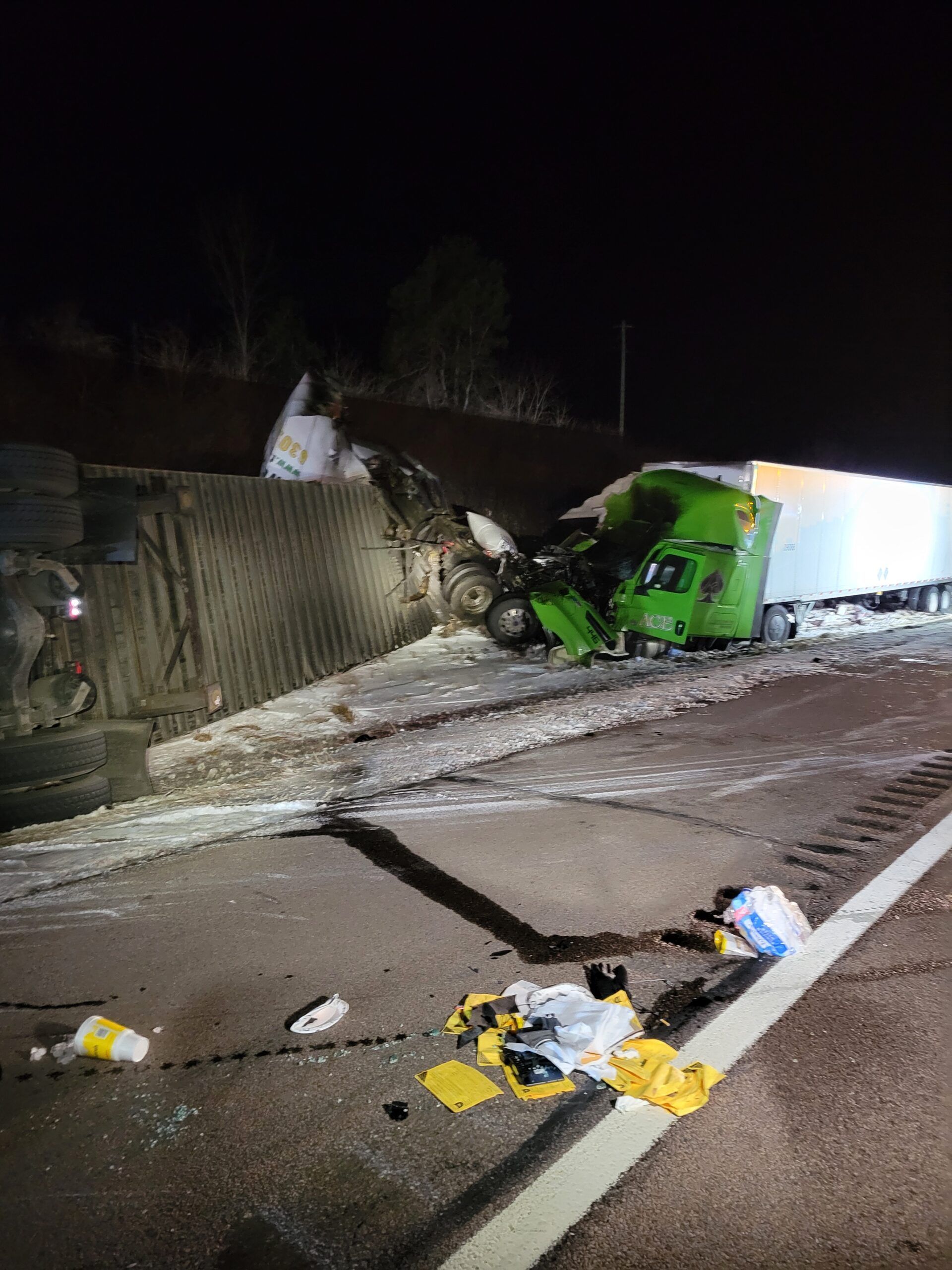 Overturned green truck after a nighttime crash, with debris scattered across a snowy road