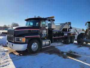 Black tow truck parked in snow beside another truck under a clear blue sky.