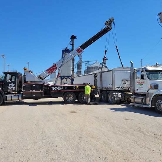 Tow truck lifting a semi-truck trailer at a construction site under a bright blue sky