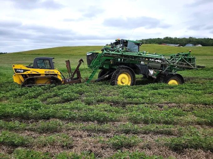 Yellow and green farm machinery in a muddy field under an overcast sky