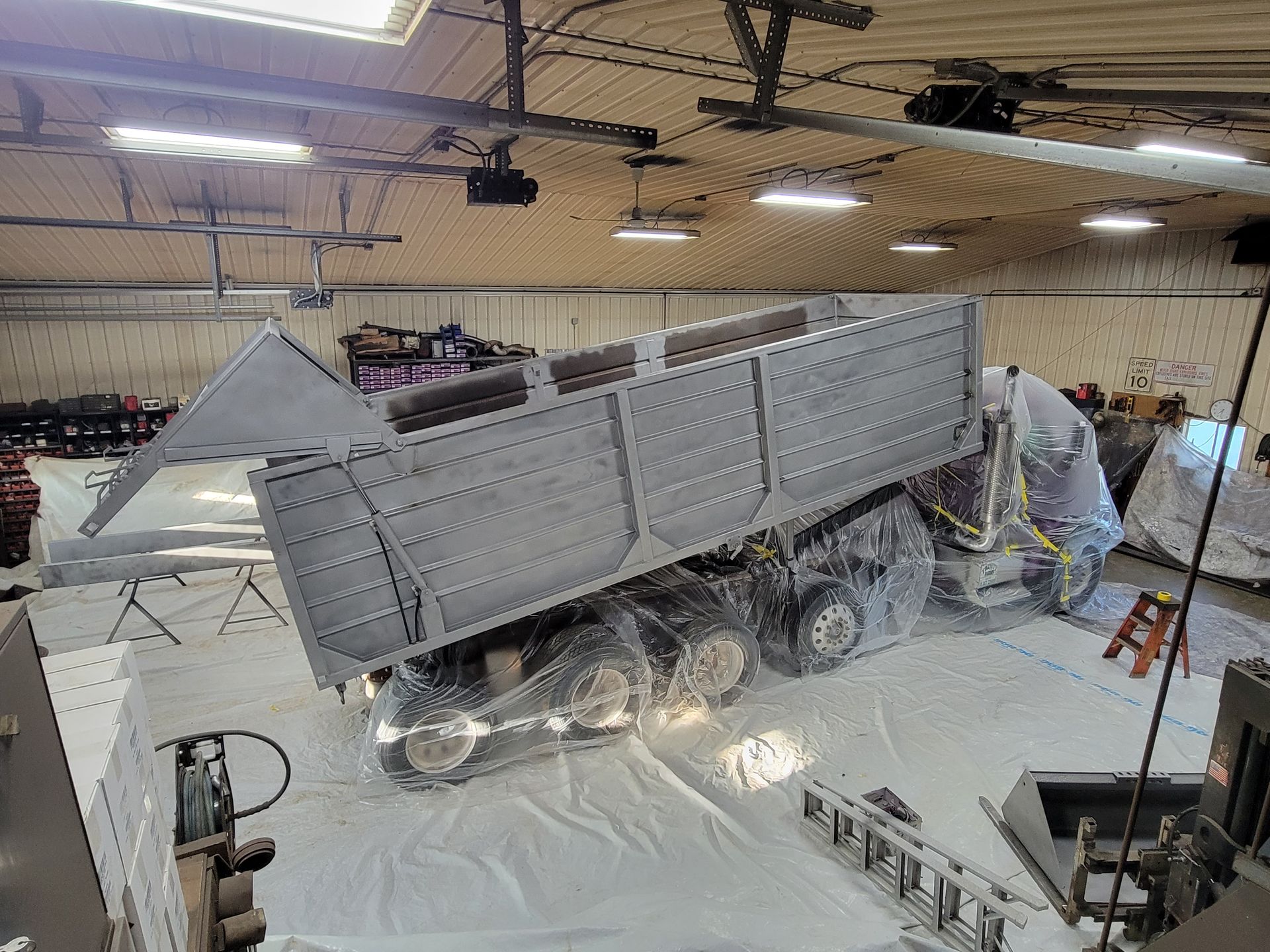 Large metallic satellite or aircraft-like structure under construction inside a warehouse, with workers nearby