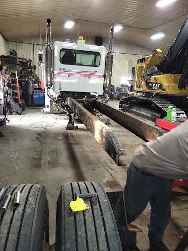 Truck in a garage with long metal beams on the floor and a worker standing beside them.