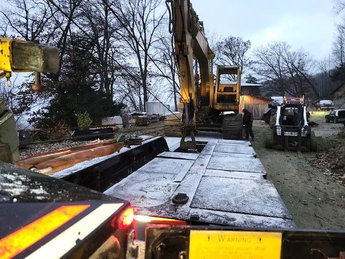 Construction site with excavator lifting concrete slabs beside a road at dusk
