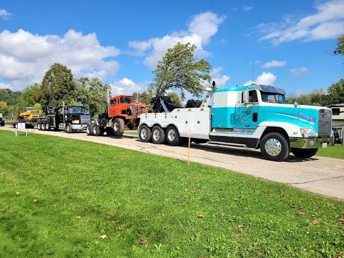 Three tow trucks parked along a road on a sunny day, with green grass and blue sky.