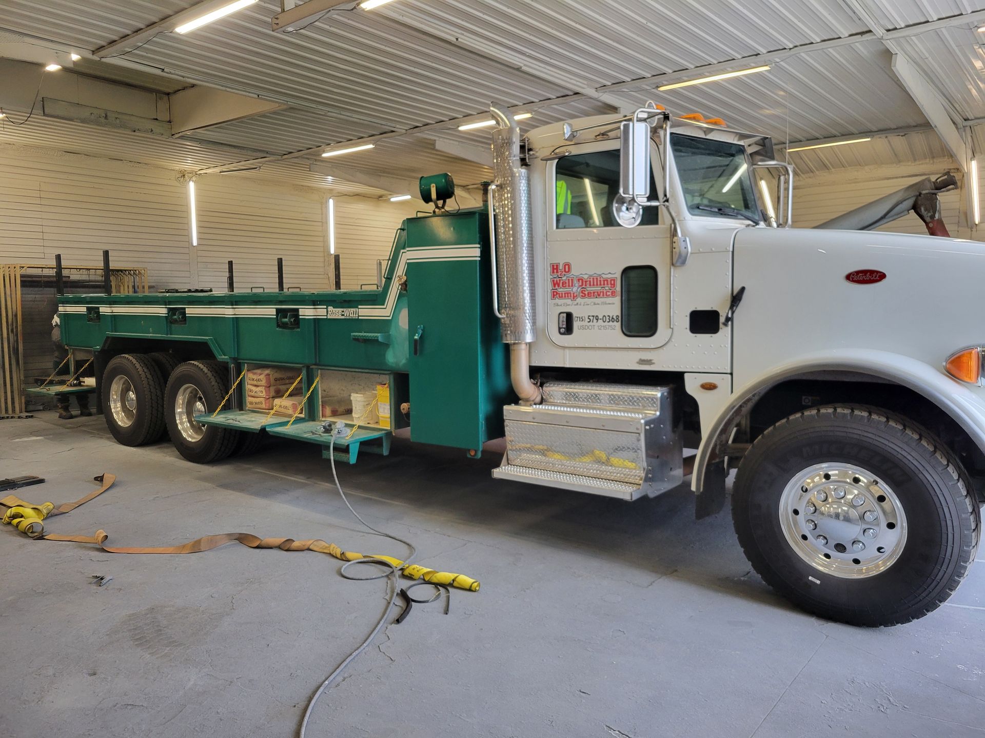 White semi-truck with green flatbed trailer parked indoors in a garage or service bay