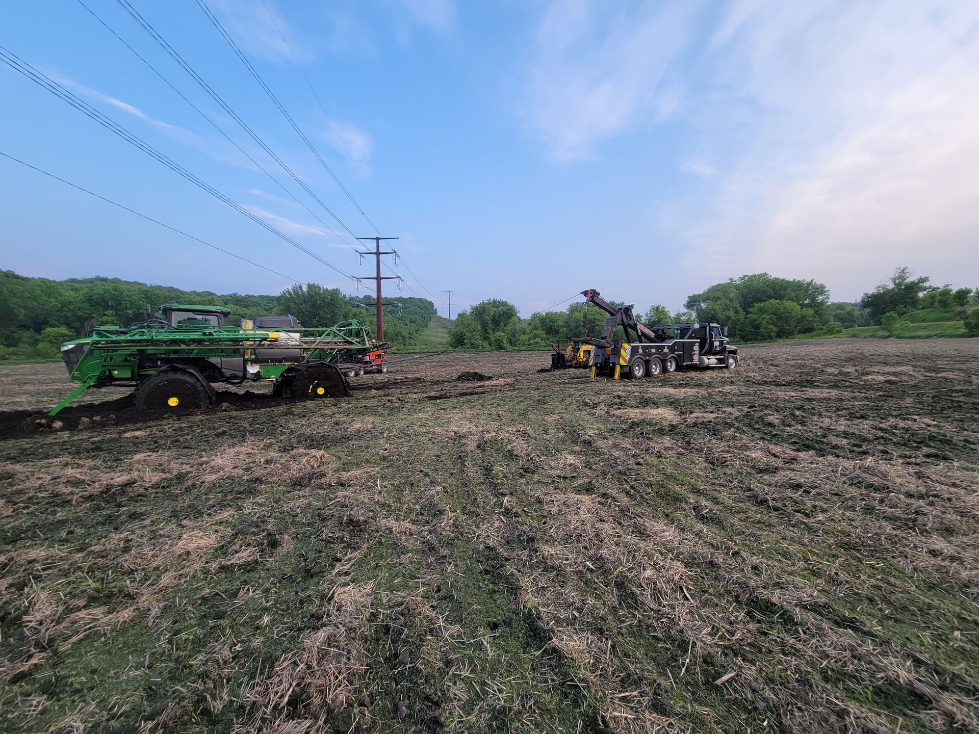 Farm field with a green tractor on the left and workers gathered near equipment on the right under a blue sky.