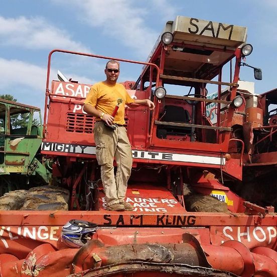 Man standing on a red farm machine with a broken engine, outdoors under a clear sky