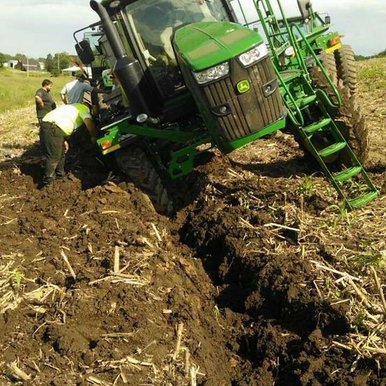 Green tractor stuck in a muddy field while people push it free