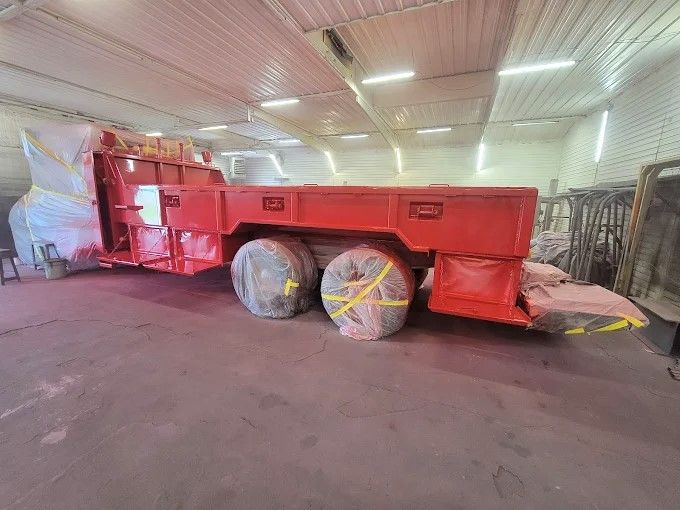 Large red industrial machine in a warehouse, with two wrapped wheels and a covered front section