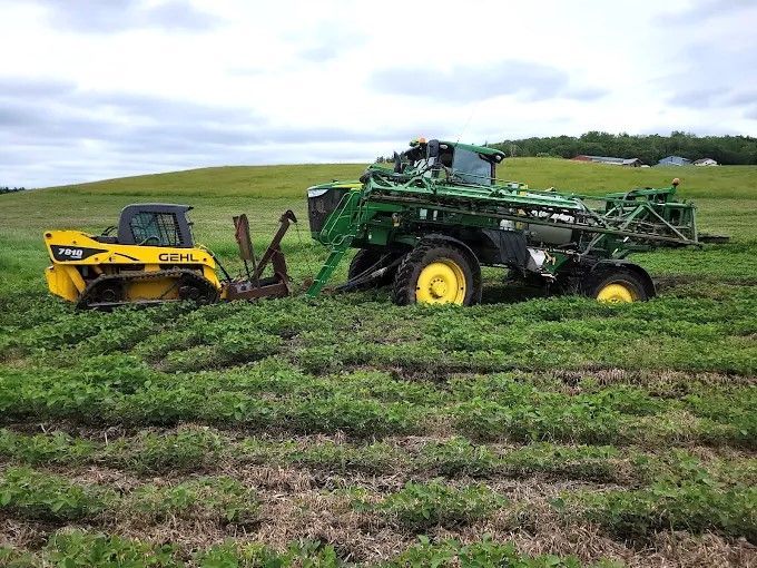 Yellow and green farm machinery working in a muddy field under a cloudy sky