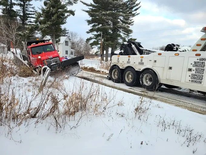 Red tow truck pulling a red SUV from a snowy ditch beside a road