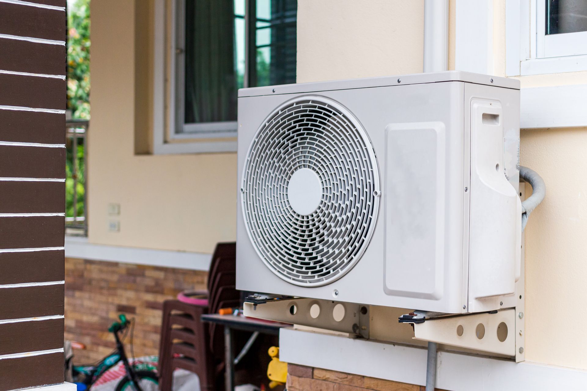 Outdoor air conditioner unit mounted on a house wall near a window and brick exterior wall Outdoor air conditioner unit mounted on a house wall near a window and brick exterior wall