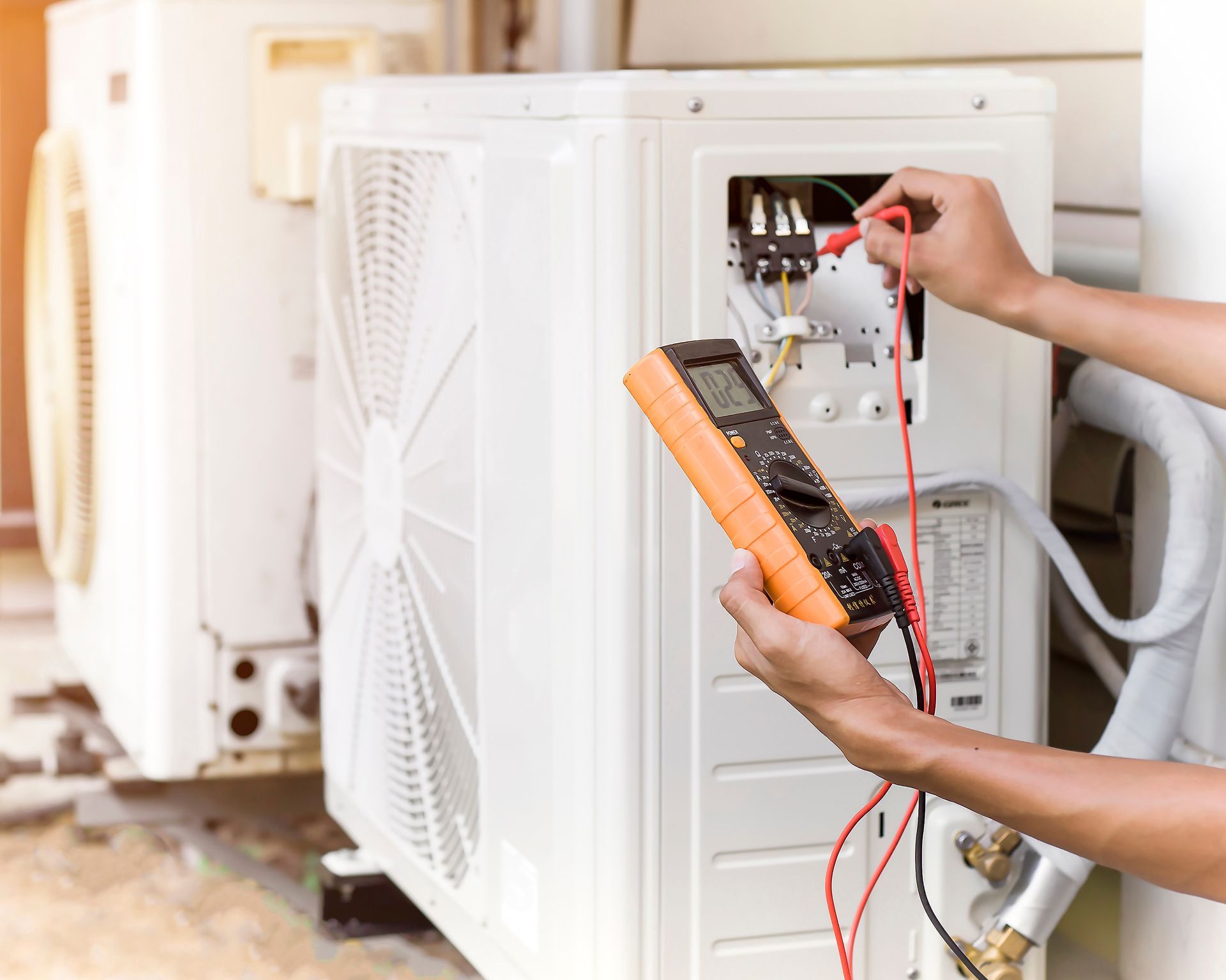 Technician testing outdoor air conditioner wiring with a multimeter
