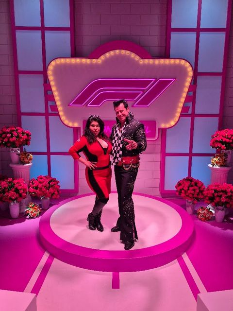 Brian Mills and his wife, Charity, pose on a pink F1-Formula 1 themed Neon Chapel with the Formula 1 logo.