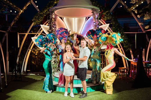 People posing with a colorful floral sculpture and trophy in an outdoor event setting