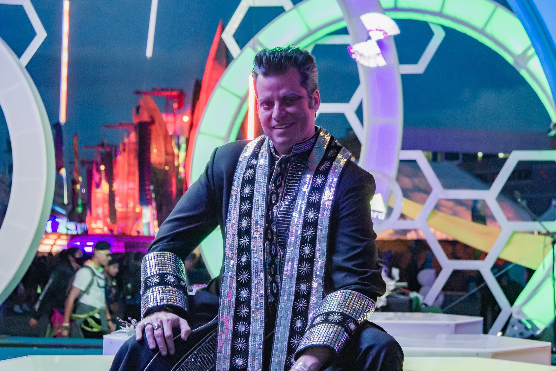 A man in a black and silver costume is sitting on a stage at EDC, the Electric Daisy Carnival