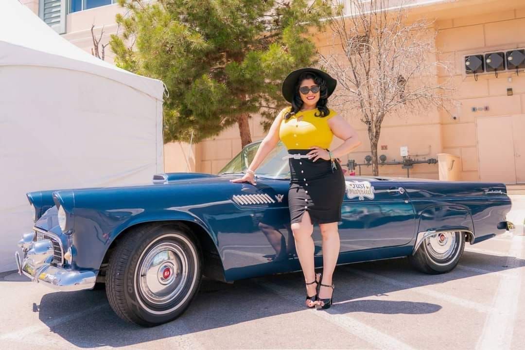 A woman is standing next to a blue car in a parking lot.