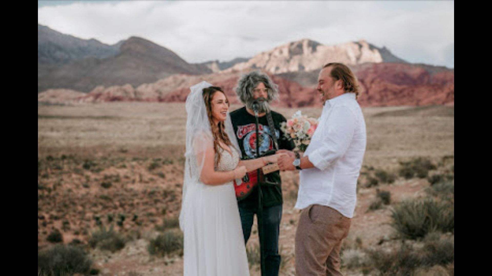 A bride and groom are getting married in the desert by a Jerry Garcia Impersonator.