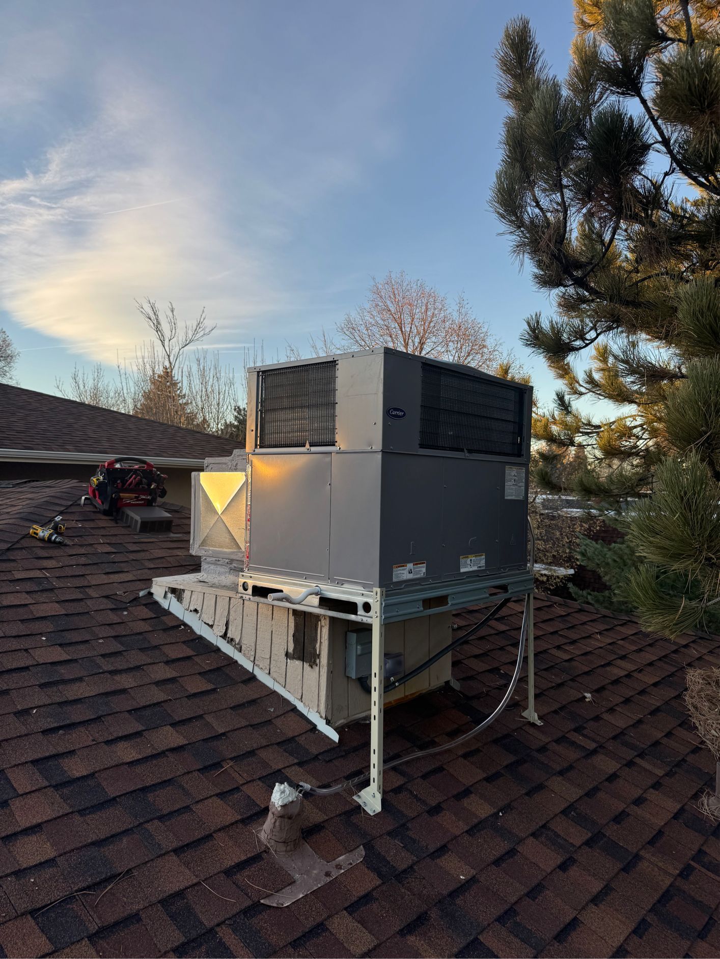 Rooftop HVAC unit on a shingled roof with a partly cloudy sky.