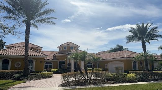 Yellow house with red tile roof and palm trees under a partly cloudy sky.