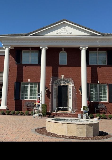 Red brick house with white columns, clear plastic covering the door, and a brick patio.