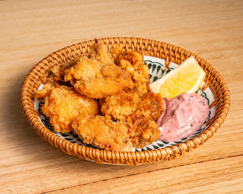 A basket filled with fried chicken and sauce on a wooden table.
