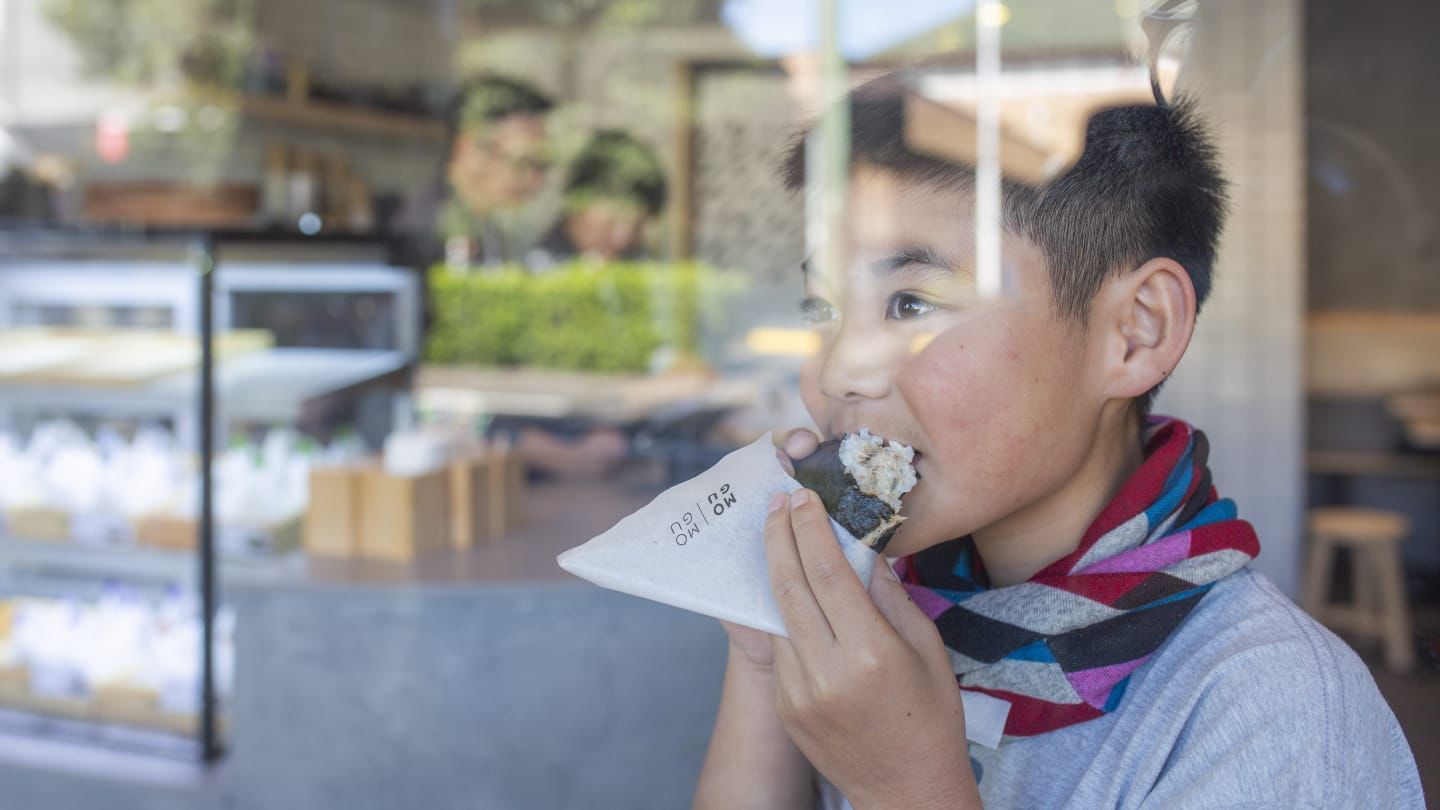 A young boy is eating onigiri in front of a window in a restaurant.