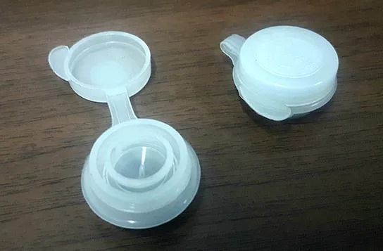 Dos tapas de plástico blancas sobre una mesa de madera, una abierta y otra cerrada.