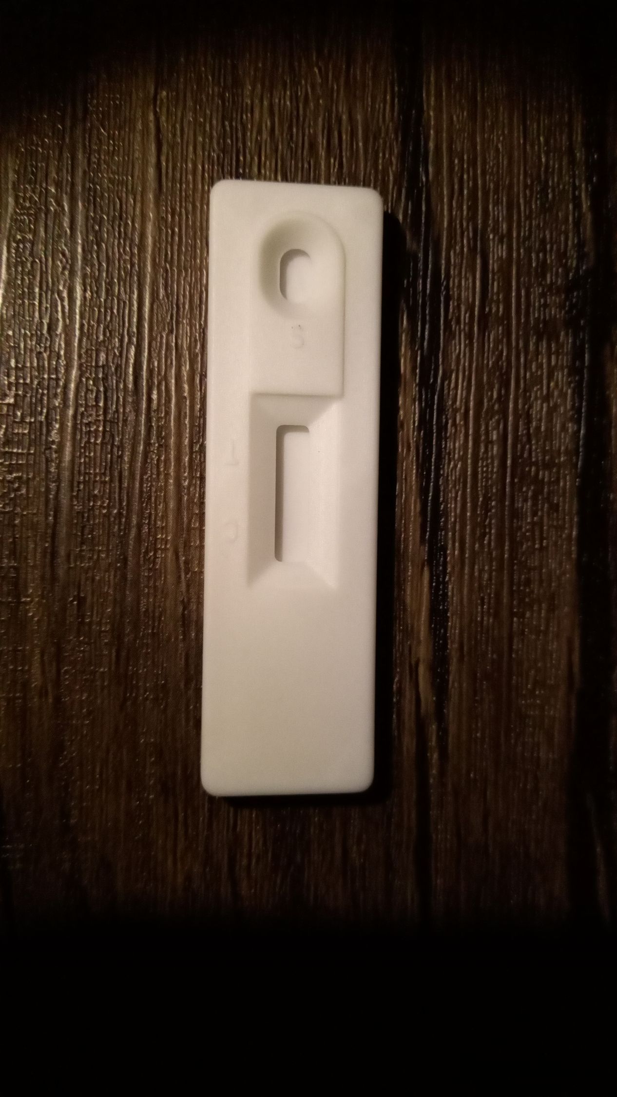 Clip de pared de plástico blanco montado sobre una superficie de madera oscura.