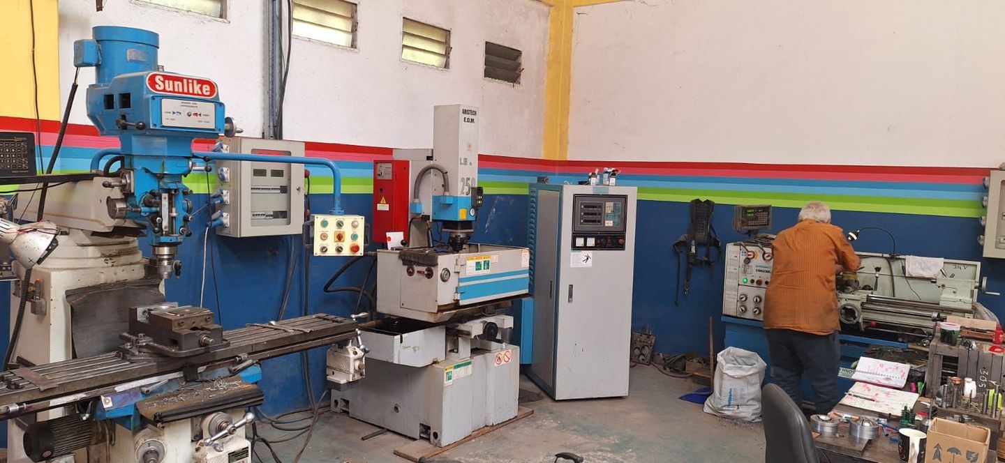 Taller industrial con maquinaria azul de gran tamaño y un trabajador con chaqueta naranja inspeccionando el equipo.