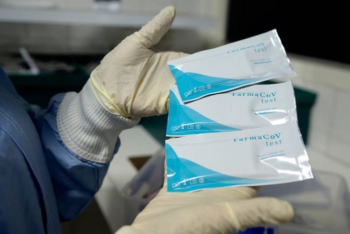 Manos enguantadas sosteniendo tres bolsas de embalaje médico estériles de color azul y blanco.