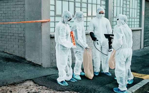 Four workers in white protective suits and masks hold bags outside a building.