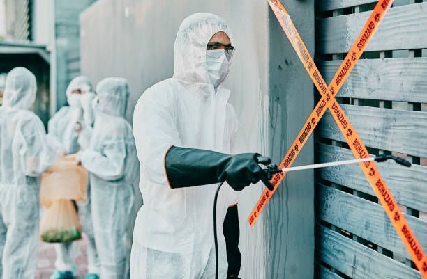 Worker in white hazmat suit and mask sealing a storefront with orange caution tape