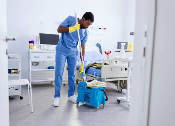 Hospital cleaner mopping floor in a patient room beside a bed and medical equipment