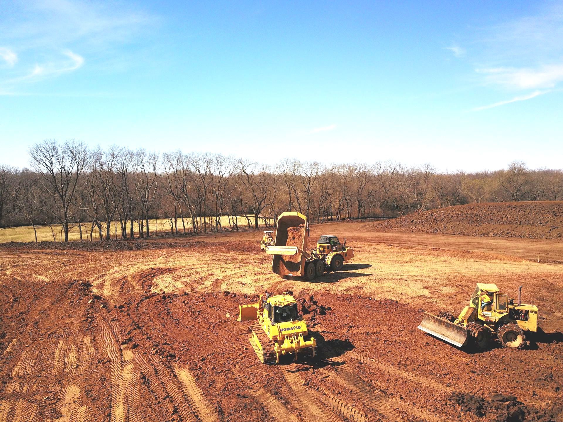 Three bulldozers are working in a dirt field.