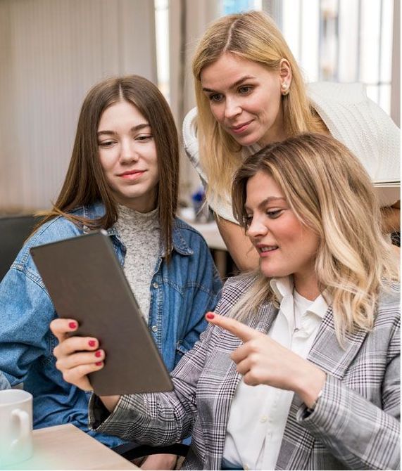 Three women looking at a tablet together, one points. Office setting.
