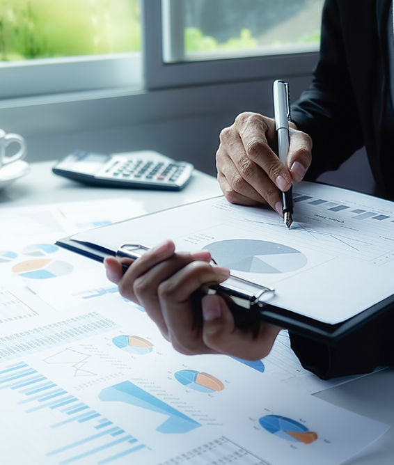 Person in suit analyzing financial charts with pen, clipboard, and calculator in a bright office setting.