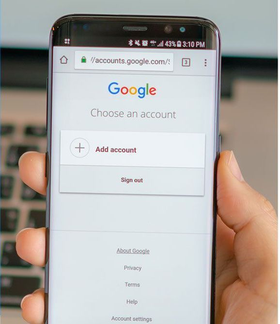 A hand holding a smartphone displaying Google's account selection page with