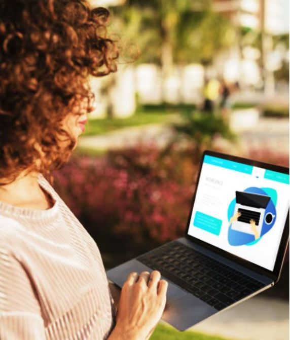 Woman with curly hair working on a laptop outdoors, browsing a website with a laptop graphic.