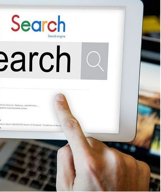 A person's finger touches a tablet screen displaying a search bar with the word