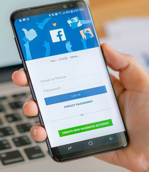 Hand holding a phone displaying the Facebook login screen with a logo and a
