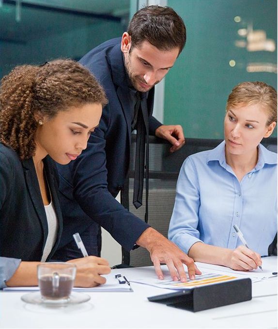 Three business colleagues reviewing paperwork, with a man pointing to a document.
