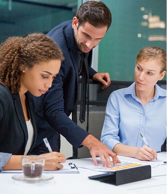 Three businesspeople reviewing documents at a table in an office.