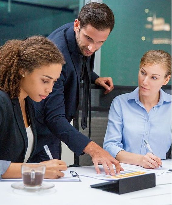 Three businesspeople reviewing documents in an office, man pointing, women writing.